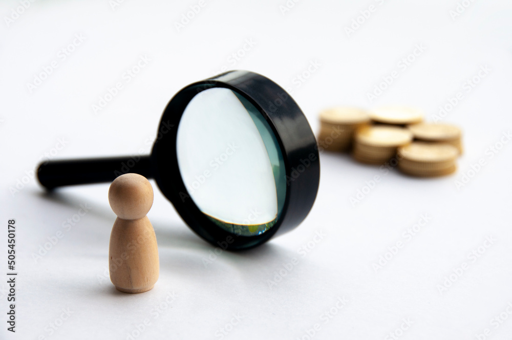 Fototapeta premium Wooden doll looking through magnifying glass for wealth. Copy space.