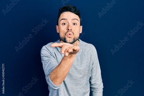 Young hispanic man wearing casual clothes looking at the camera blowing a kiss with hand on air being lovely and sexy. love expression.