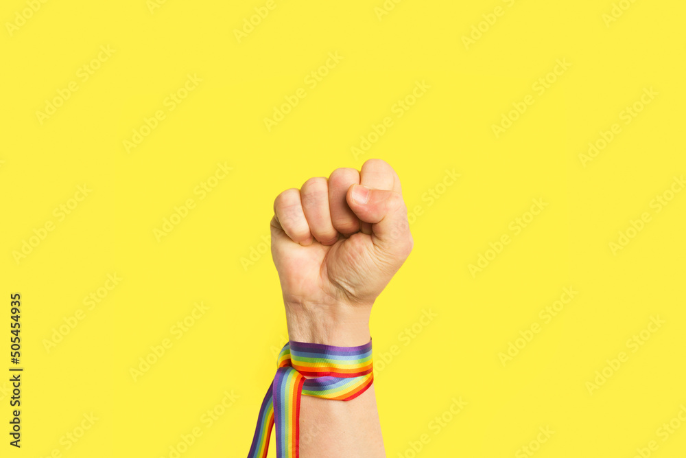 Ταπετσαρία Puño levantado con pulsera de bandera arcoíris LGBT sobre un fondo amarillo brillante liso y aislado