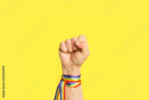 Puño levantado con pulsera de bandera arcoíris LGBT sobre un fondo amarillo brillante liso y aislado. Vista de frente y de cerca. Copy space