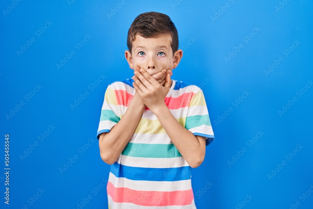 Young caucasian kid standing over blue background shocked covering mouth with hands for mistake. secret concept. Young caucasian kid standing over blue background shocked covering mouth with hands for mistake. secret concept.