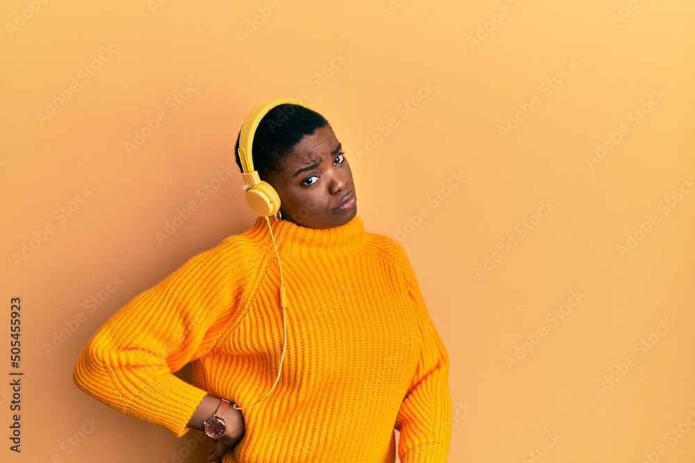 Beautiful african american young woman with short hair wearing headphones listening to music and dancing over isolated yellow background Beautiful african american young woman with short hair wearing headphones listening to music and dancing over isolated yellow background