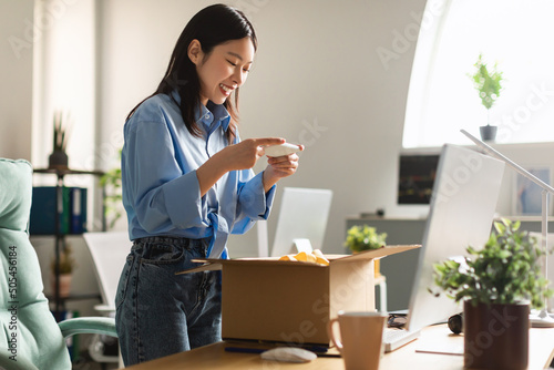 Happy Asian woman packing parcel and taking photo of box photo