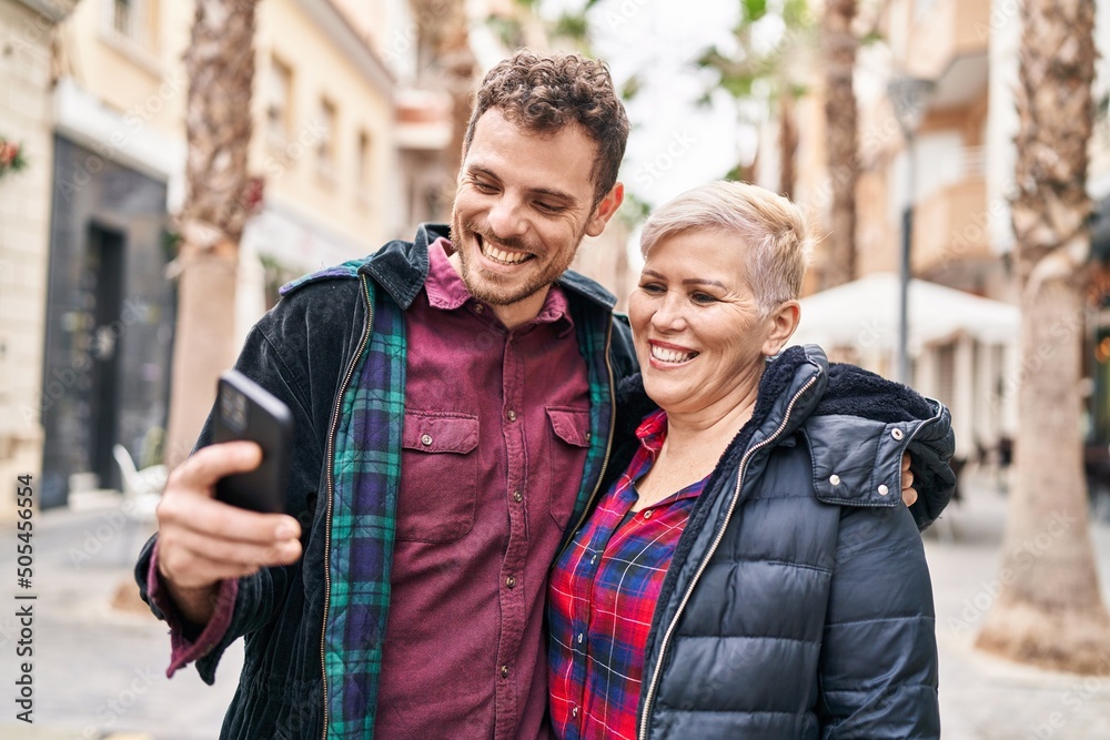 Mother and son smiling confident using smartphone at street