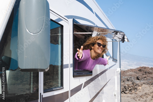 Portrait of beautiful smiling curly woman wearing glasses and violet sweater traveling in motorhome camper looking out the window happy. Caucasian woman enjoying free lifestyle, vacation, travel