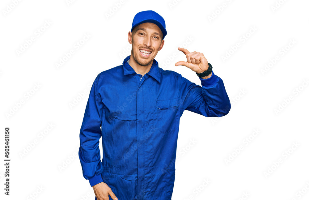 Bald man with beard wearing builder jumpsuit uniform smiling and confident gesturing with hand doing small size sign with fingers looking and the camera. measure concept.