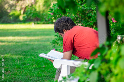 A man reads a book in a green summer park on a white bench
