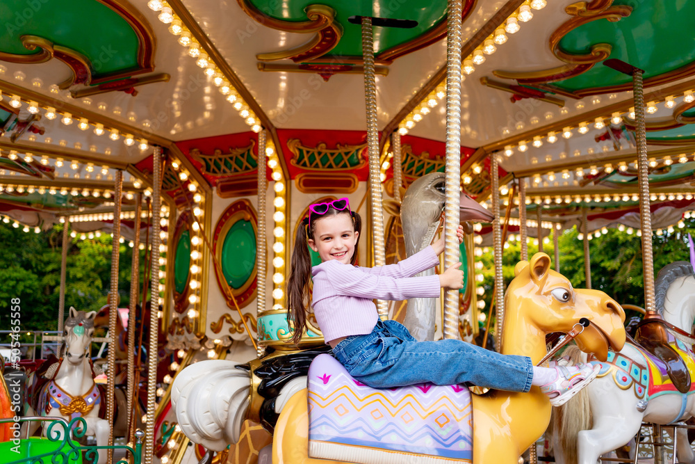 a child girl in an amusement park rides on a carousel and smiles with happiness, the concept of weekends and school holidays