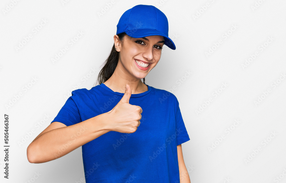 Young hispanic girl wearing delivery courier uniform doing happy thumbs up gesture with hand. approving expression looking at the camera showing success.