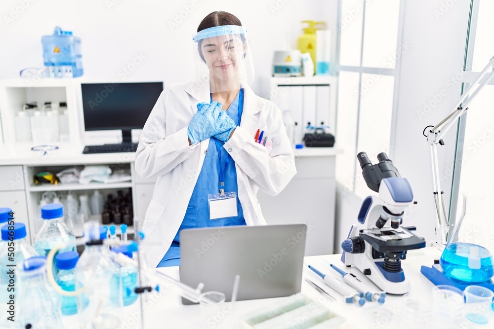 Young hispanic woman wearing scientist uniform smiling with hands on chest with closed eyes and grateful gesture on face. health concept.