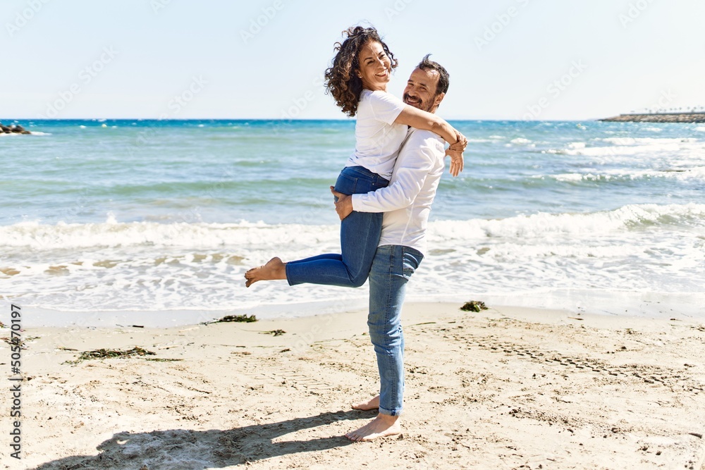 Middle age hispanic couple smiling happy and hugging at the beach.