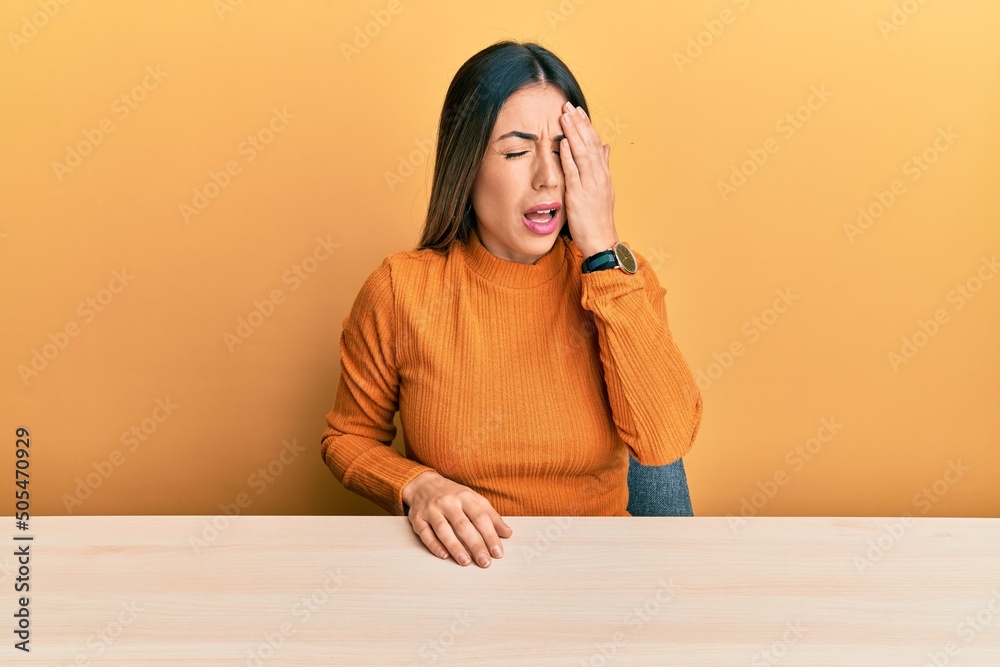 Young hispanic woman wearing casual clothes sitting on the table yawning tired covering half face, eye and mouth with hand. face hurts in pain. Young hispanic woman wearing casual clothes sitting on the table yawning tired covering half face, eye and mouth with hand. face hurts in pain.