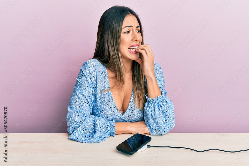 Φωτογραφία Young hispanic woman wearing casual clothes charging smartphone battery looking stressed and nervous with hands on mouth biting nails