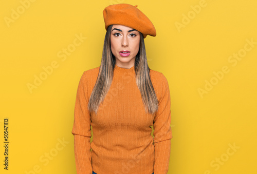 Young hispanic woman wearing french look with beret with serious expression on face. simple and natural looking at the camera.