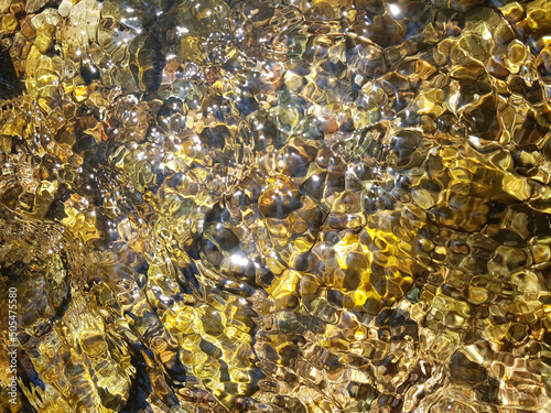 Selective focus shot of beach pebbles under clear water with sunrays photo