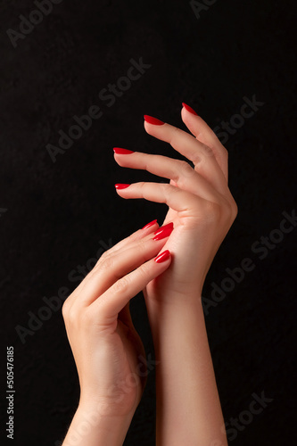Photography Female hands with beautiful manicure - red nails on dark black background