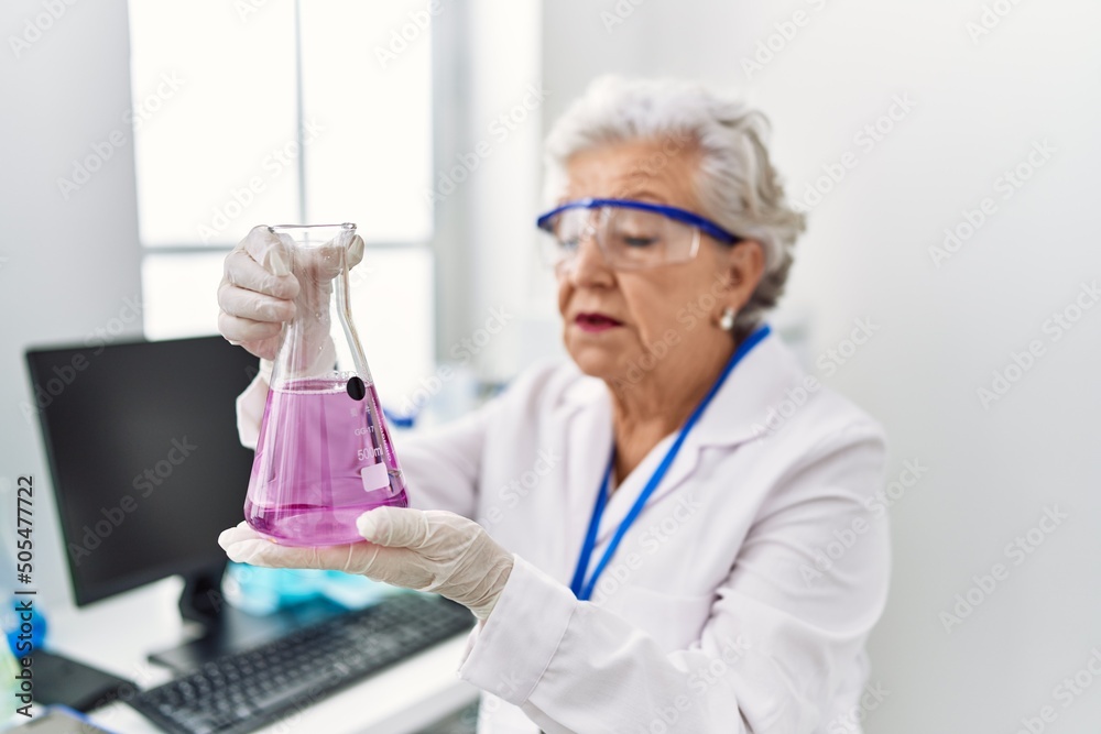 Senior grey-haired woman wearing scientist uniform holding test tube at laboratory Senior grey-haired woman wearing scientist uniform holding test tube at laboratory