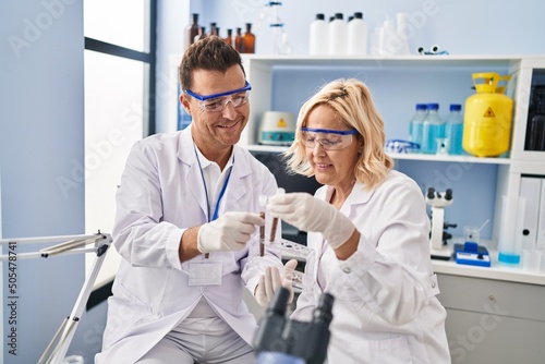 Middle age man and woman scientist partners holding test tube working at laboratory