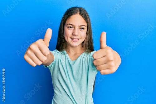 Beautiful brunette little girl wearing casual white t shirt approving doing positive gesture with hand, thumbs up smiling and happy for success. winner gesture. © Krakenimages.com