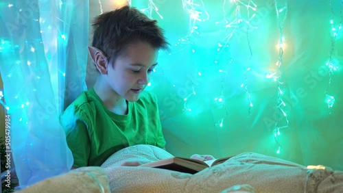 a teenager in an elf costume reads a book sitting on a bed decorated with garlands. reading a book on Christmas night