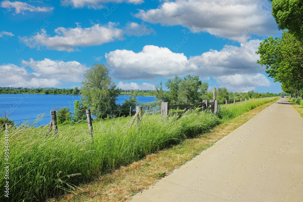Beautiful scenic rural dutch landscape , river Maas lake, cycle track, green trees, blue sky - Ohe en Laak, Netherlands Beautiful scenic rural dutch landscape , river Maas lake, cycle track, green trees, blue sky - Ohe en Laak, Netherlands