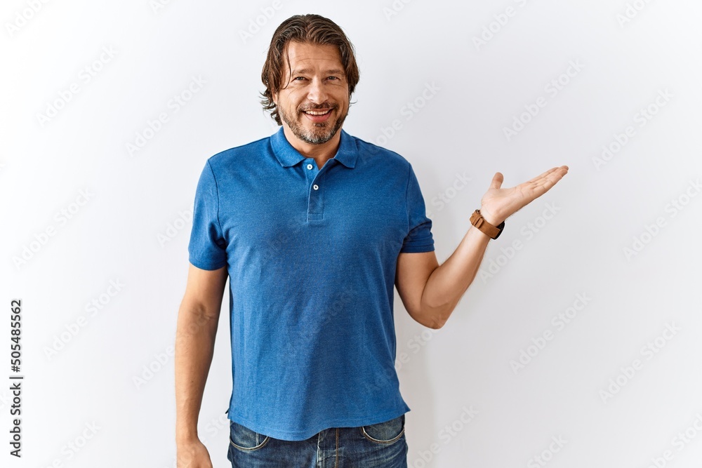 Handsome middle age man standing together over isolated background smiling cheerful presenting and pointing with palm of hand looking at the camera.