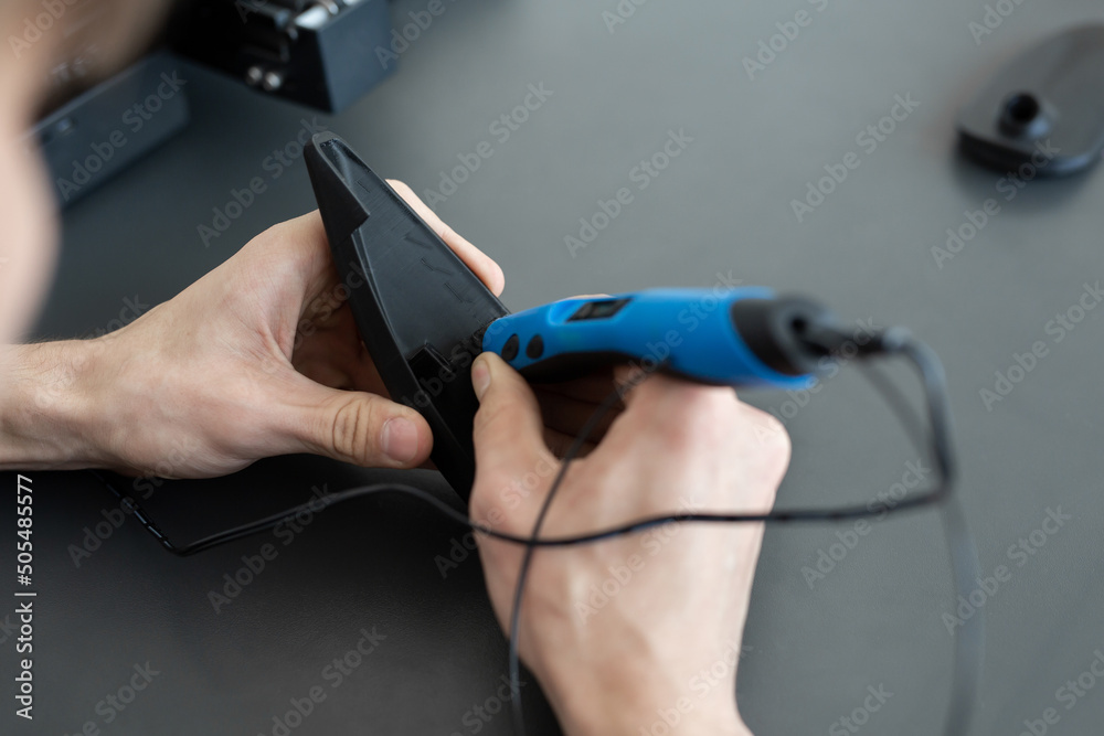 Man connects two 3D printer parts with a 3D pen Man connects two 3D printer parts with a 3D pen