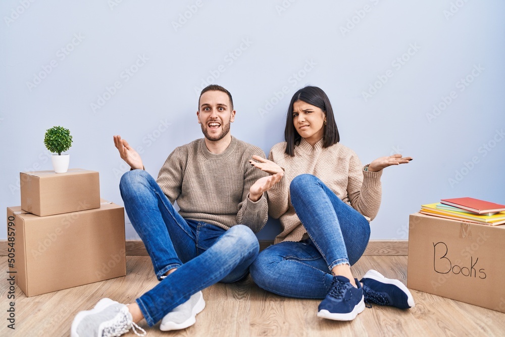 Young couple moving to a new home clueless and confused with open arms, no idea concept.