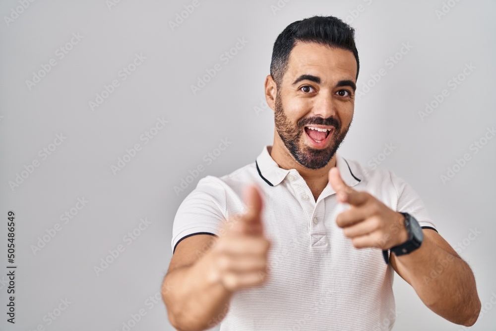 Young hispanic man with beard wearing casual clothes over white background pointing fingers to camera with happy and funny face. good energy and vibes. Young hispanic man with beard wearing casual clothes over white background pointing fingers to camera with happy and funny face. good energy and vibes.