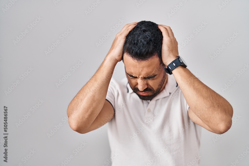 Young hispanic man with beard wearing casual clothes over white background suffering from headache desperate and stressed because pain and migraine. hands on head. Young hispanic man with beard wearing casual clothes over white background suffering from headache desperate and stressed because pain and migraine. hands on head.