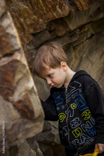 A boy-child on the background of a rocky mountain looks at something with curiosity and is surprised. Nature, rocks, mountains.