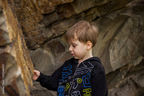 A boy-child on the background of a rocky mountain looks at something with curiosity and is surprised. Nature, rocks, mountains.