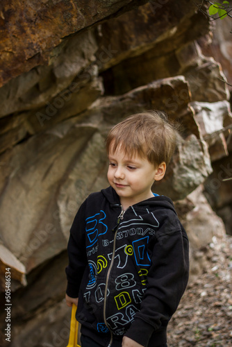 A boy-child on the background of a rocky mountain looks at something with curiosity and is surprised. Nature, rocks, mountains.