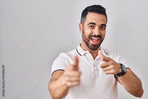 Young hispanic man with beard wearing casual clothes over white background pointing fingers to camera with happy and funny face. good energy and vibes.