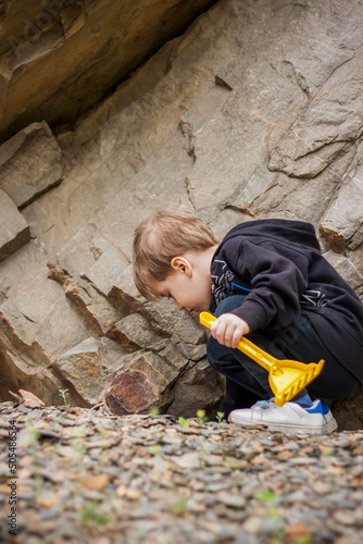 A boy-child on the background of a rocky mountain looks at something with curiosity and is surprised. Nature, rocks, mountains.