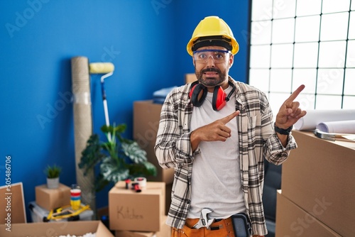 Young hispanic man with beard working at home renovation pointing aside worried and nervous with both hands, concerned and surprised expression