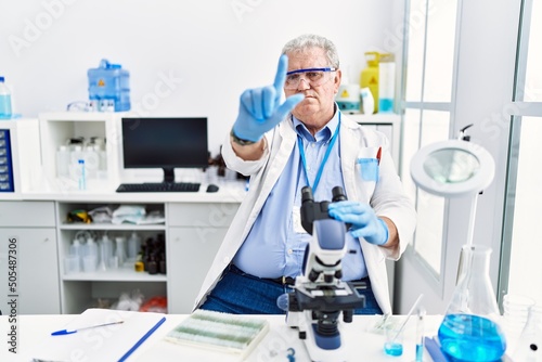 Senior caucasian man working at scientist laboratory pointing with finger up and angry expression  showing no gesture
