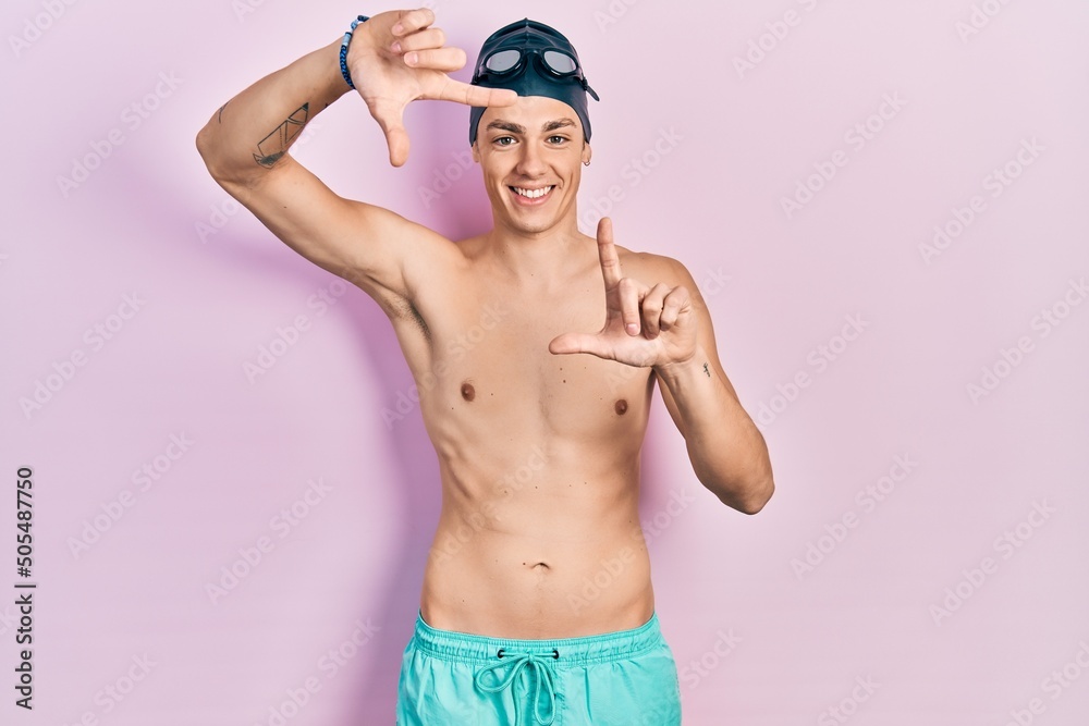 Young hispanic man wearing swimwear and swimmer glasses smiling making frame with hands and fingers with happy face. creativity and photography concept.