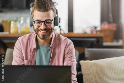 A handsome young man in the headphones with a smartphone in his hand using a laptop computer. Online banking photo