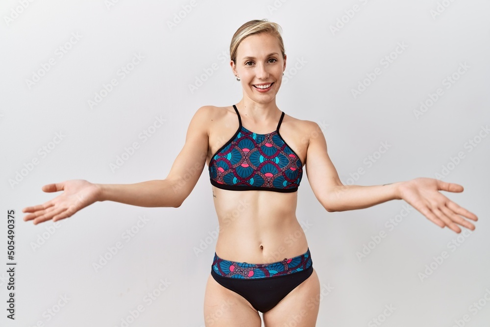 Young blonde woman wearing sporty bikini over isolated background smiling cheerful with open arms as friendly welcome, positive and confident greetings Young blonde woman wearing sporty bikini over isolated background smiling cheerful with open arms as friendly welcome, positive and confident greetings