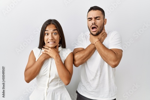 Young interracial couple standing together in love over isolated background shouting and suffocate because painful strangle. health problem. asphyxiate and suicide concept.