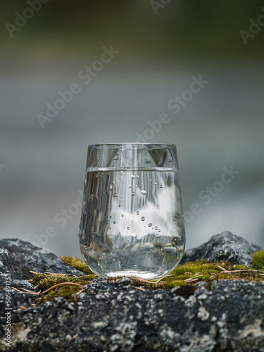 Closeup shot of a glass cup of water on a rocky surface reflecting a rounf with blurred background photo