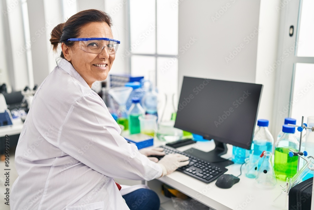 Middle age hispanic woman wearing scientist uniform using computer at laboratory Middle age hispanic woman wearing scientist uniform using computer at laboratory