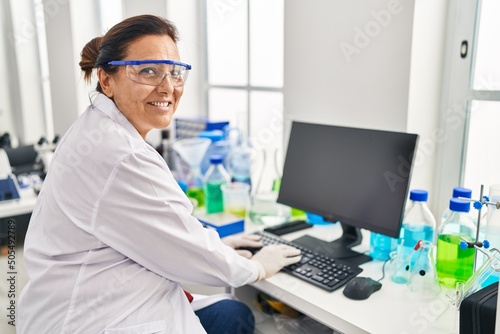 Middle age hispanic woman wearing scientist uniform using computer at laboratory
