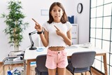 Young hispanic girl standing at pediatrician clinic pointing aside worried and nervous with both hands, concerned and surprised expression