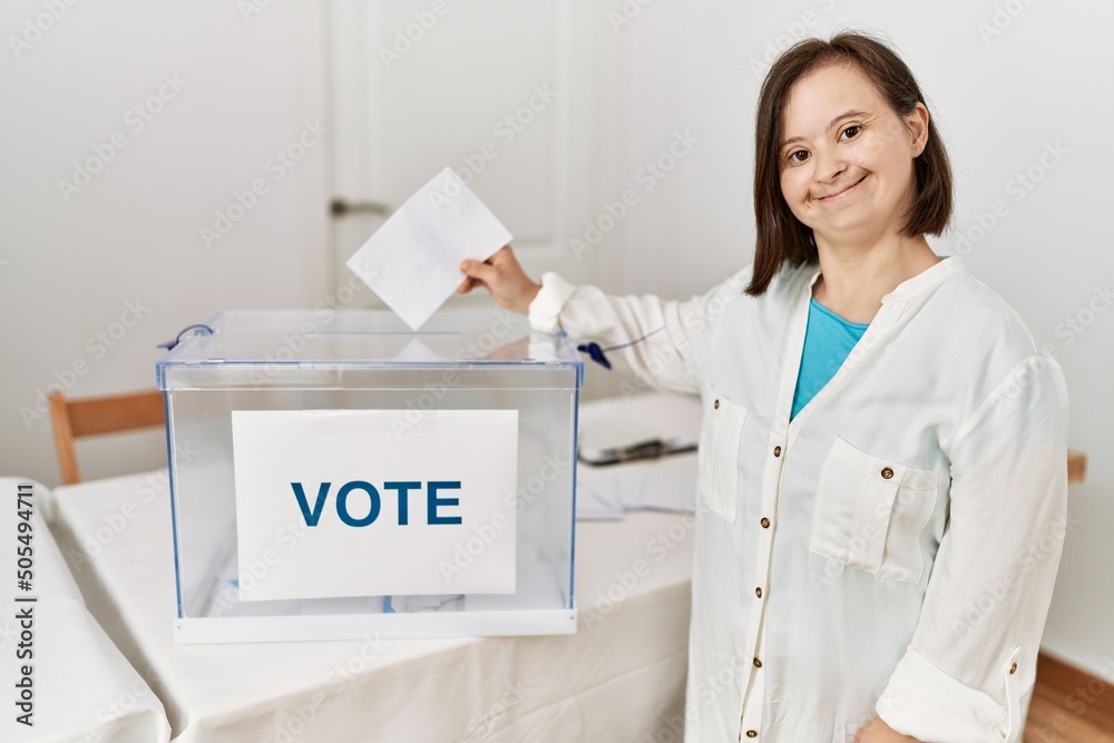 Brunette woman with down syndrome smiling putting envelope in ballot box at election room Brunette woman with down syndrome smiling putting envelope in ballot box at election room