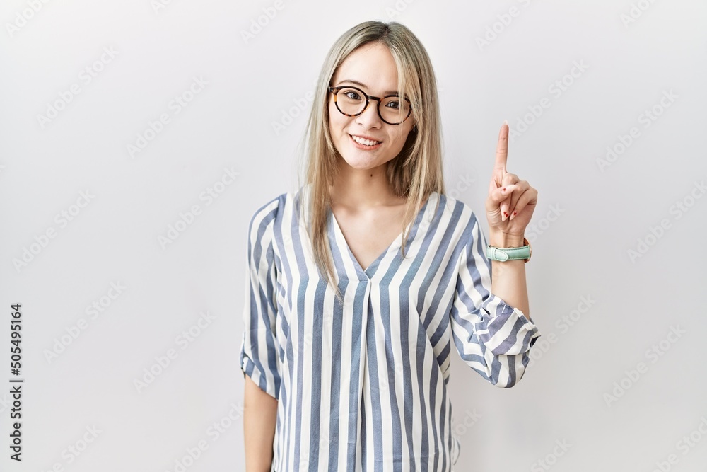 Obraz premium Asian young woman wearing casual clothes and glasses showing and pointing up with finger number one while smiling confident and happy.