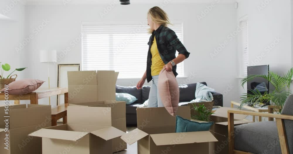 Happy diverse female couple talking and holding boxes during moving home