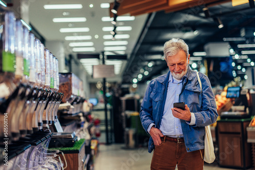 Senior man using phone while shopping in grocery