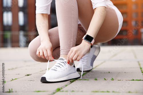 Obraz na plátně Close up woman beginner runner tie laces on sneakers, sitting on feet, on city s